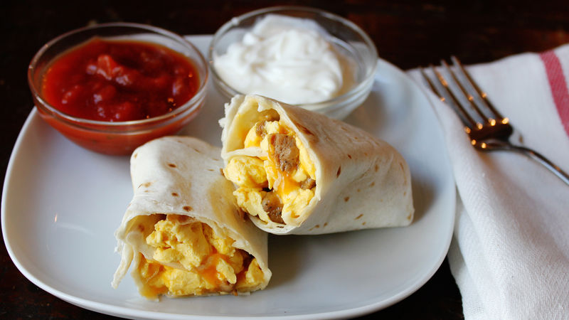 A breakfast burrito on a plate with salsa and sour cream